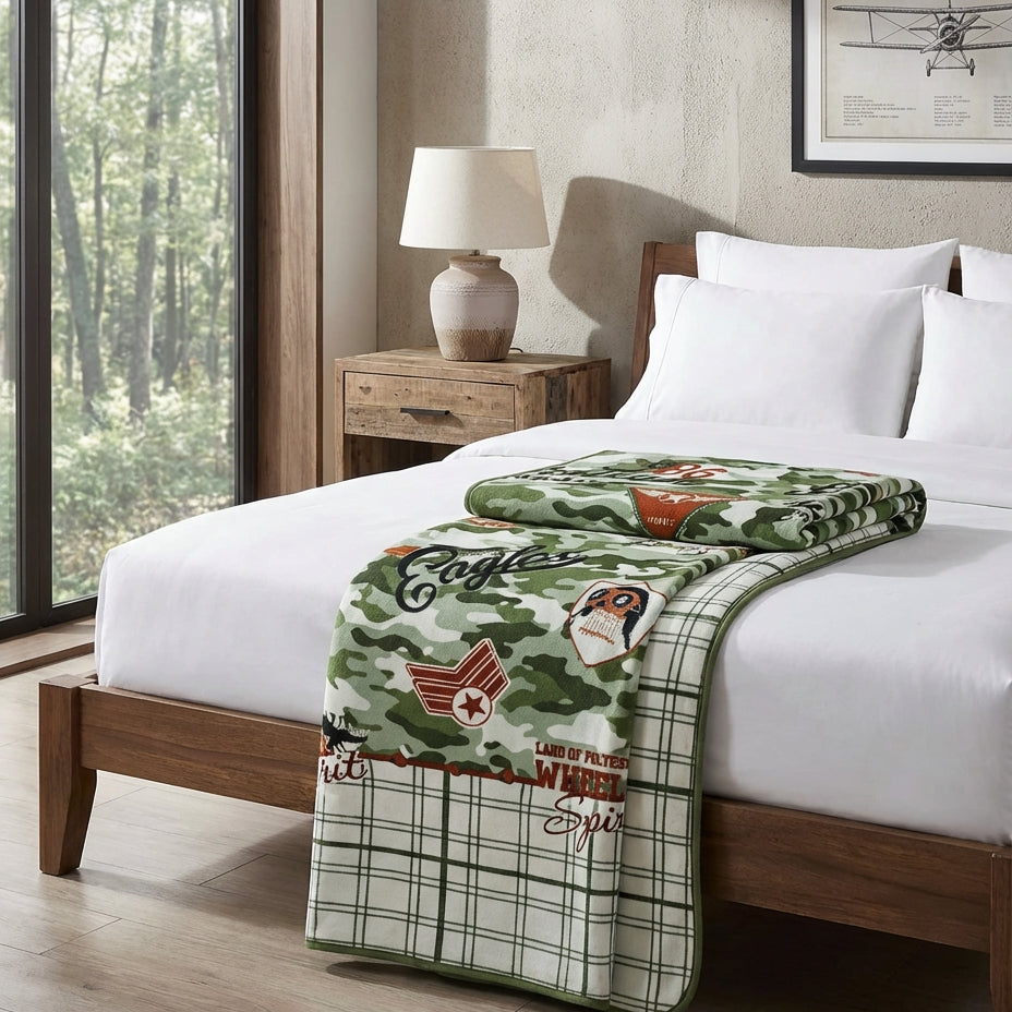 Bedroom with a bed featuring a green and white blanket with logos, a wooden nightstand, and a lamp.